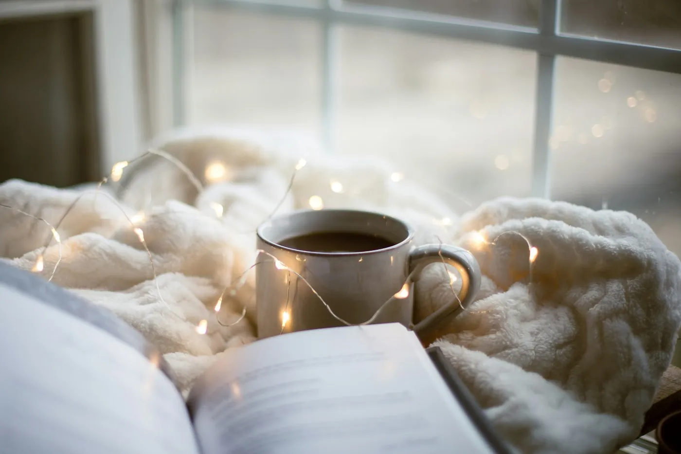A cup of coffee and an open book on a soft blanket