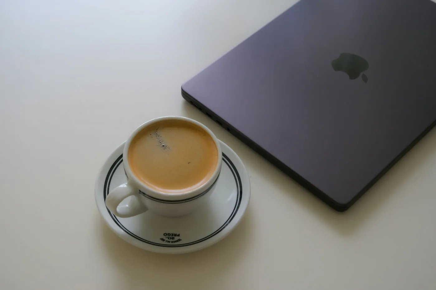 An espresso beside a closed laptop on a white table